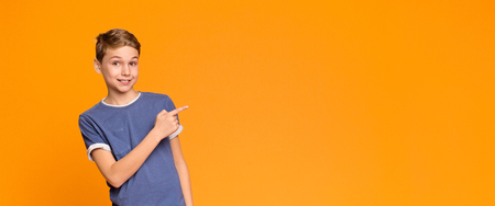 Wow, look. Emotional teen boy pointing aside at empty space, orange panorama backgroundの写真素材