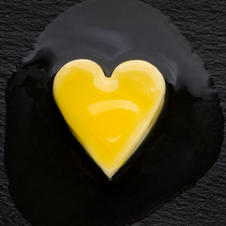 Heart-shaped piece of butter melting on black pan. High cholesterol foods conceptの写真素材