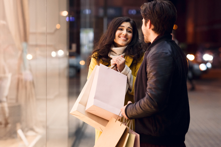 Shopping together. Girl asking boyfriend to buy clothes, walking near shop windowsの写真素材