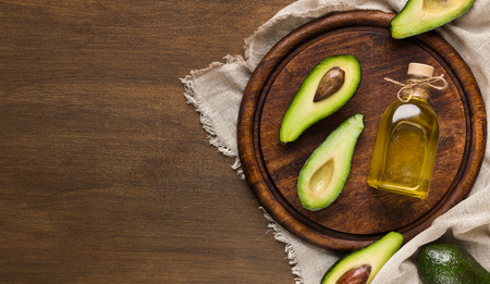 Avocado halves and bottle of oil on cutting board over wooden background top view, copy space. Vegetarian nutrition conceptの写真素材