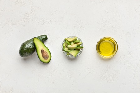 Whole and sliced avocado and oil in bowls on concrete background top view. Super healthy food...