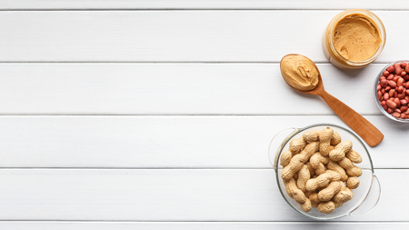 Peanut butter in jar and spoon and bowls of peanuts on white wooden background, top view, copy spaceの写真素材