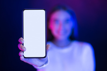 Girl showing blank smartphone screen over neon studio background, blue and pink lightsの写真素材