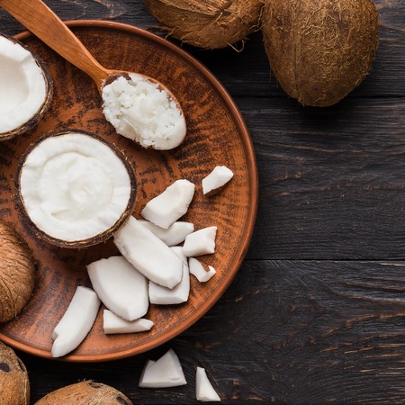 Coconut pieces, flesh and butter on plate over wooden background, top view. Cooking with coconut...