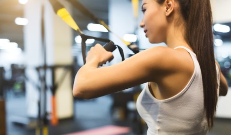 TRX exercises. Girl training with trx straps in the gym, closeup