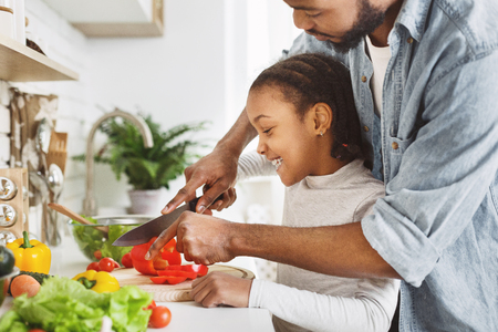 Afro ameriacan father cutting vegetables with little daughter, cooking saladの写真素材