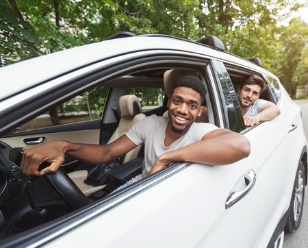 Happy millennials friends traveling by car, looking out open car window