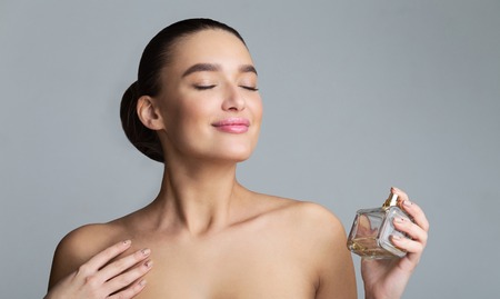 Beautiful Woman Spraying Perfume On Her Neck Over Grey Background