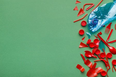 Crampled plastic bottle in fish shape and plastic trash on green background, top view, copy space. Save ocean conceptの写真素材