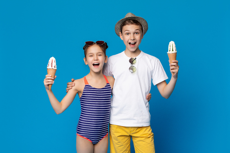 Summer snack. Two kids smiling and holding ice cream cones, blue studio backgroundの写真素材