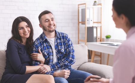 Young cheerful millennial couple at consultation with personal psychologist, free spaceの写真素材