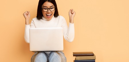 Yeah, I Passed Exam! Happy Student Girl With Books And Laptop Over Light Studio Backgroundの写真素材