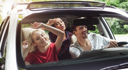 Happy young friends traveling by car, listening to music and singing, having fun