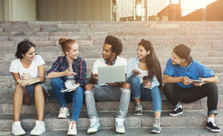 Multiethnic teen friends communicating outdoors, discussing interesting things on campus staircase, empty spaceの写真素材