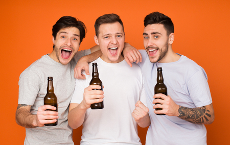Hurray, weekend! Men Holding Beer Bottles Over Orange Studio Backgroundの写真素材