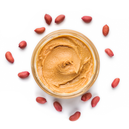 Open jar of peanut butter and scattered peanuts on white background, top view. Unhealthy spread...