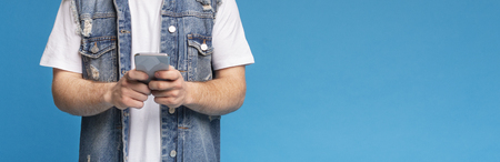 Internet searching concept. Unrecognizable young man blogger holding cellphone, writing comments and posting new photo, panorama, copy spaceの写真素材