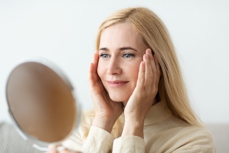 Looking At Mirror. Woman Touching Her Face And Smilingの写真素材