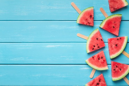 Healthy treat for kids. Watermelon triangles on wooden sticks, blue wood background