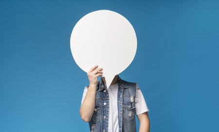 Unrecognizable man hiding his face behind blank speech bubble on blue background, free spaceの写真素材