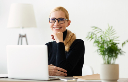 Happy Mature Businesswoman Working On Laptop At Home Office And Looking At Cameraの写真素材