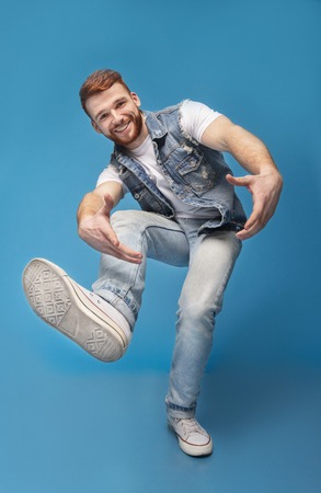 Come on! Smiling millennial caucasian guy fool around and marked out with hands at camera, full length, blue studio backgroundの写真素材