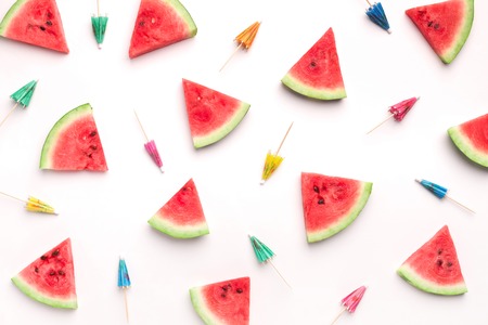 Creative summer pattern. Fresh watermelon slices and colorful paper cocktail umbrellas on whiteの写真素材