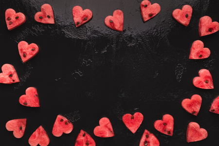 Summer love backdrop. Watermelon hearts frame on black background, top view with empty spaceの写真素材