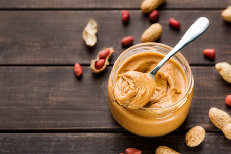 Peanut butter in jar and spoon and scattered peanuts on wooden background. American dessert concept, copy spaceの写真素材