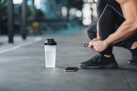 Man tying shoe laces on sneakers in gym, preparing for workout, empty spaceの写真素材