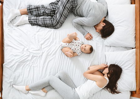 Young family in bed. Little baby lying in the middle of bed, parents sleeping on sides, top viewの写真素材