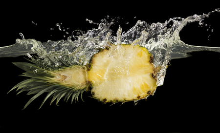Half of ripe cut pineapple dropped in water, black panorama backgroundの写真素材