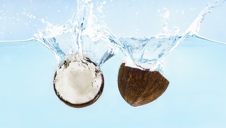 Cracked coconut with splashes falling in water, blue backgroundの写真素材