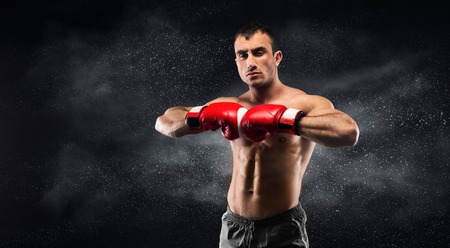 Concentrated boxer preparing for training and posing on camera on black background, copy space