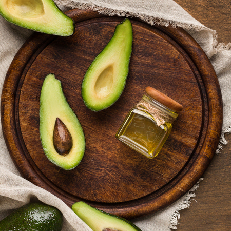 Avocado halves and jar of oil on round board over wooden background top view. Vegetarian eating conceptの写真素材