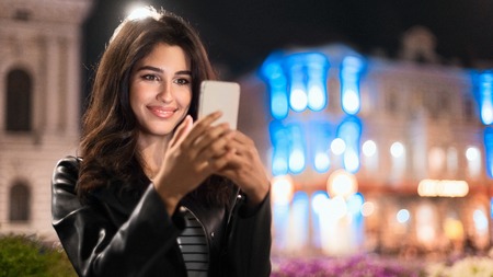 Woman checking social networks, walking at night in the city, copy space, panoramaの写真素材