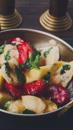 Fruit salad with strawberries served in copper bowl on wooden table, vertical panoramaの写真素材