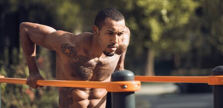 Muscular Guy Doing Street Workout, Exercising On Parallel Bars Outdoors