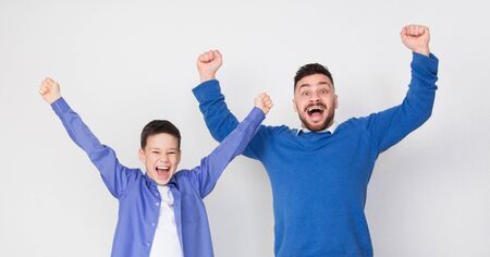 Hooray! Emotional excited father and son cheering for victory, celebrating success together, panorama, studio shotの写真素材