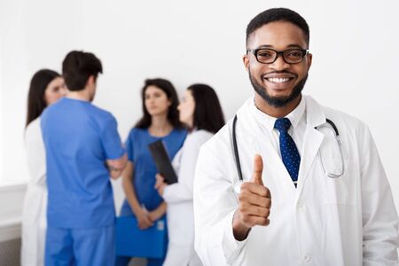 Professional African Doctor Showing Thumb Up In Front Of Medical Team In Hospitalの写真素材