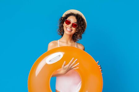 Happy millennial african woman ready for beach party, holding orange inflatable ring and smiling,...