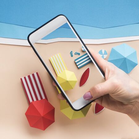 Photos from vacation. Woman holding cellphone with beautiful view of sandy beach and ocean, paper...
