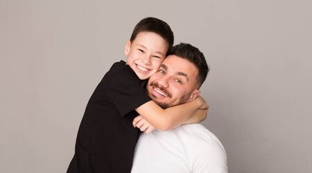 I love you, dad! Cheerful boy hugging with his father, happy family portrait, gray studio background