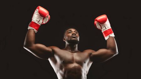 Winner. African naked athlete raising hands in boxing gloves, black panorama backgroundの写真素材