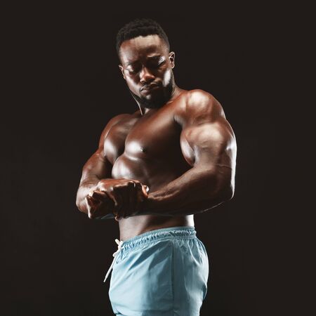 African bodybuilder flexing his muscles, showing biceps in studio, black background