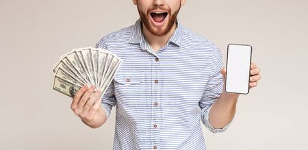 Happy millennial man with dollars and phone with blank space on studio background, panoramaの写真素材