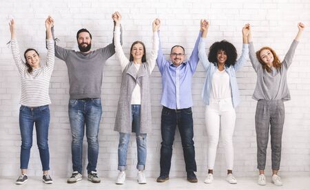 Group of successful friendly people raising connected hands, white brick wall backgroundの写真素材