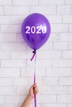 Violet balloon in woman hand on white bricks background, vertical panorama, copy spaceの写真素材
