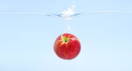 Red apple falling deeply under water with splash, blue backgroundの写真素材