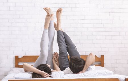 Relaxing legs up. Young couple lying on bed and raising legs in air, empty spaceの写真素材